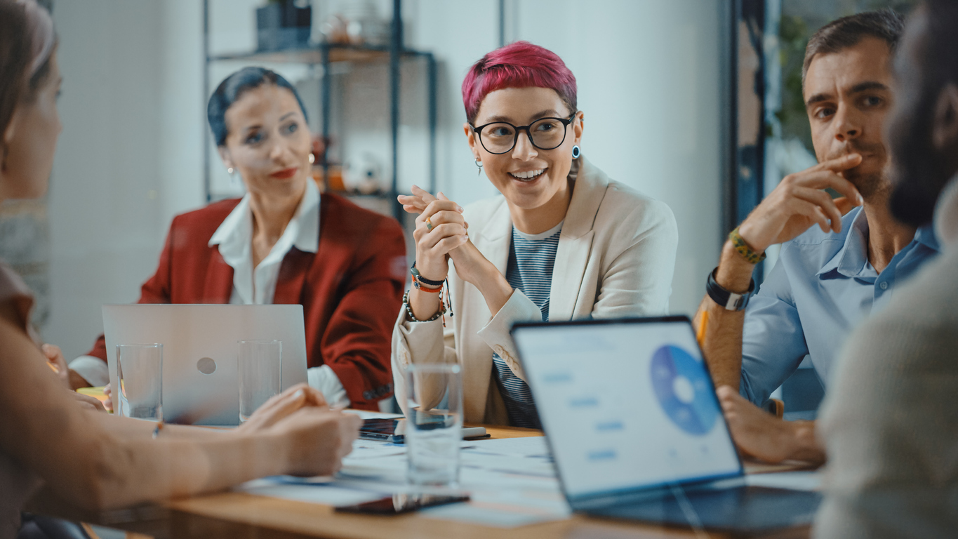 Office Meeting in Conference Room: Beautiful Specialist with Short Pink Hair Talks about Firm Strategy with Diverse Team of Professional Businesspeople. Creative Start-up Team Discusses Big Project