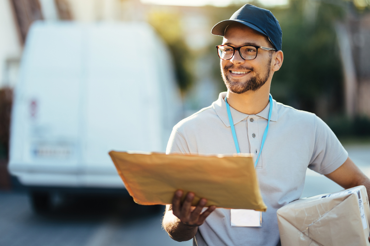 Smiling courier walking down the street and looking for right address for package delivery.