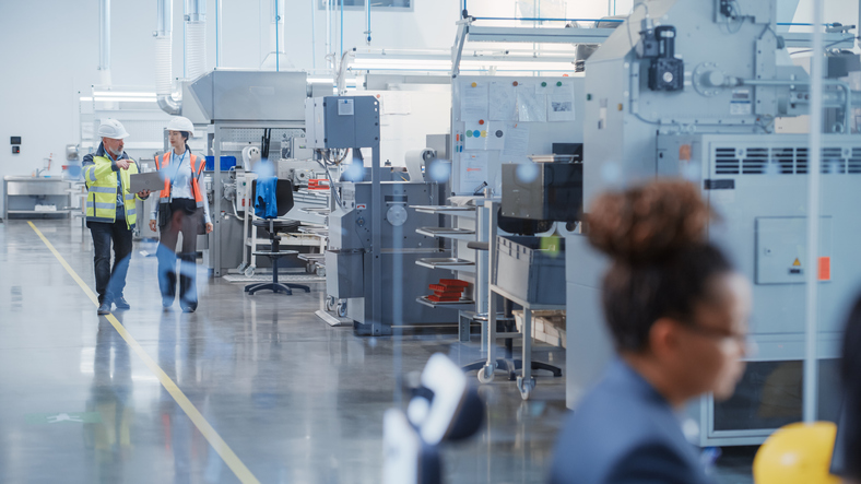 two professional heavy industry specialists in safety uniform and hard hats walking and talking in a factory. african american engineer working in the foreground