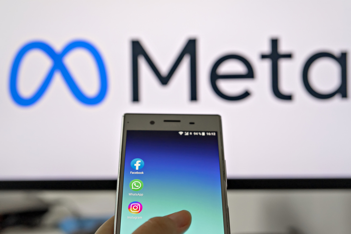 mobile display with logo of facebook, whatsapp and instagram apps in hand against blurred meta logotype on white monitor