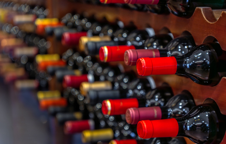 several bottles of black red wine with red labels aligned and stacked horizontally on wooden shelves and bottle racks in a private luxury wine collection.