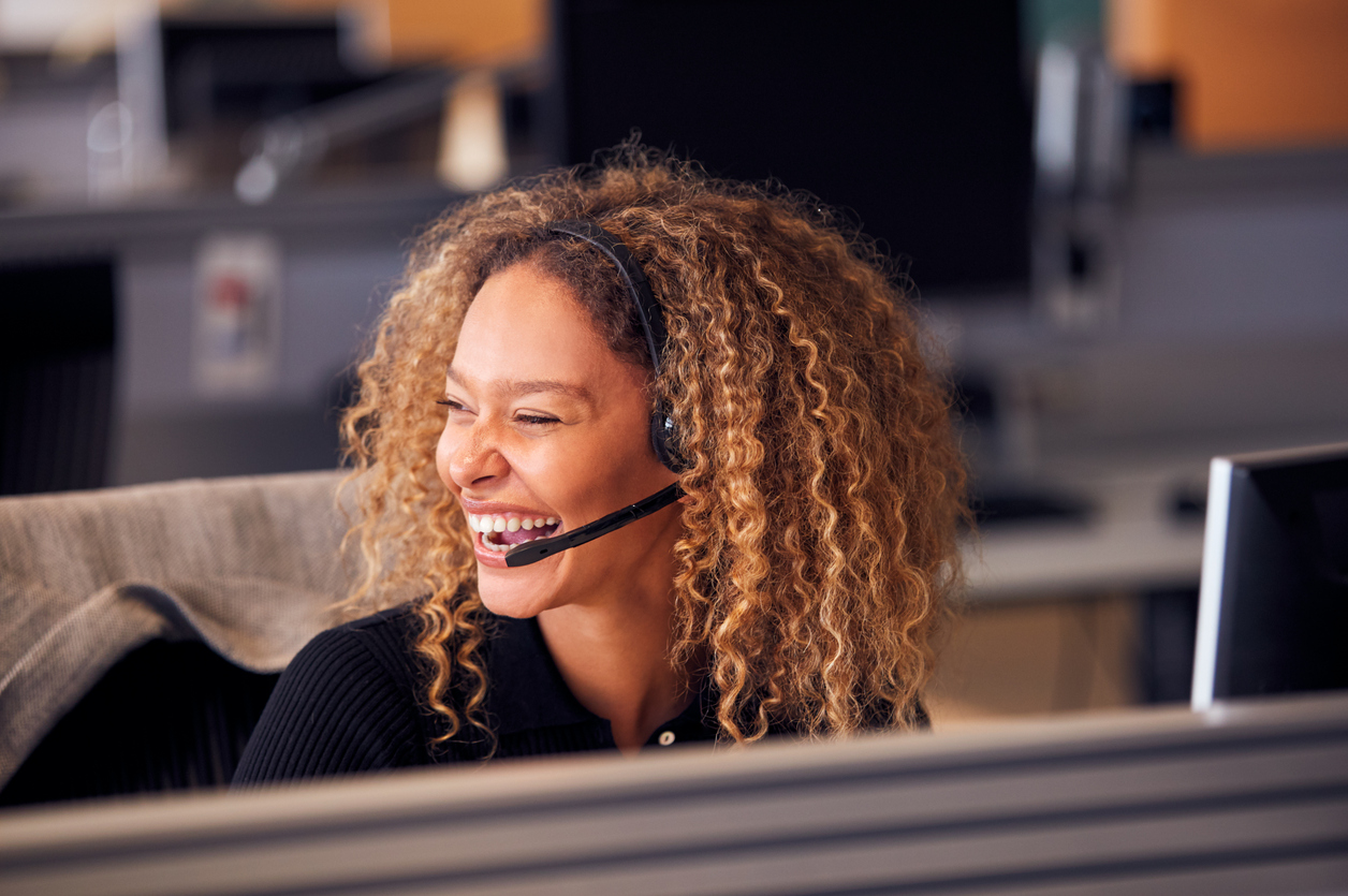 laughing businesswoman wearing telephone headset talking to caller in customer services department