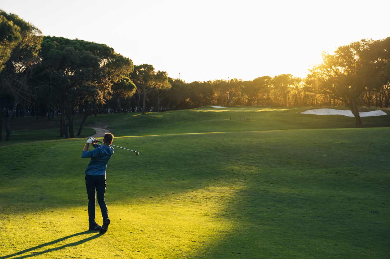 male golf player teeing off golf ball from tee box to beautiful sunset